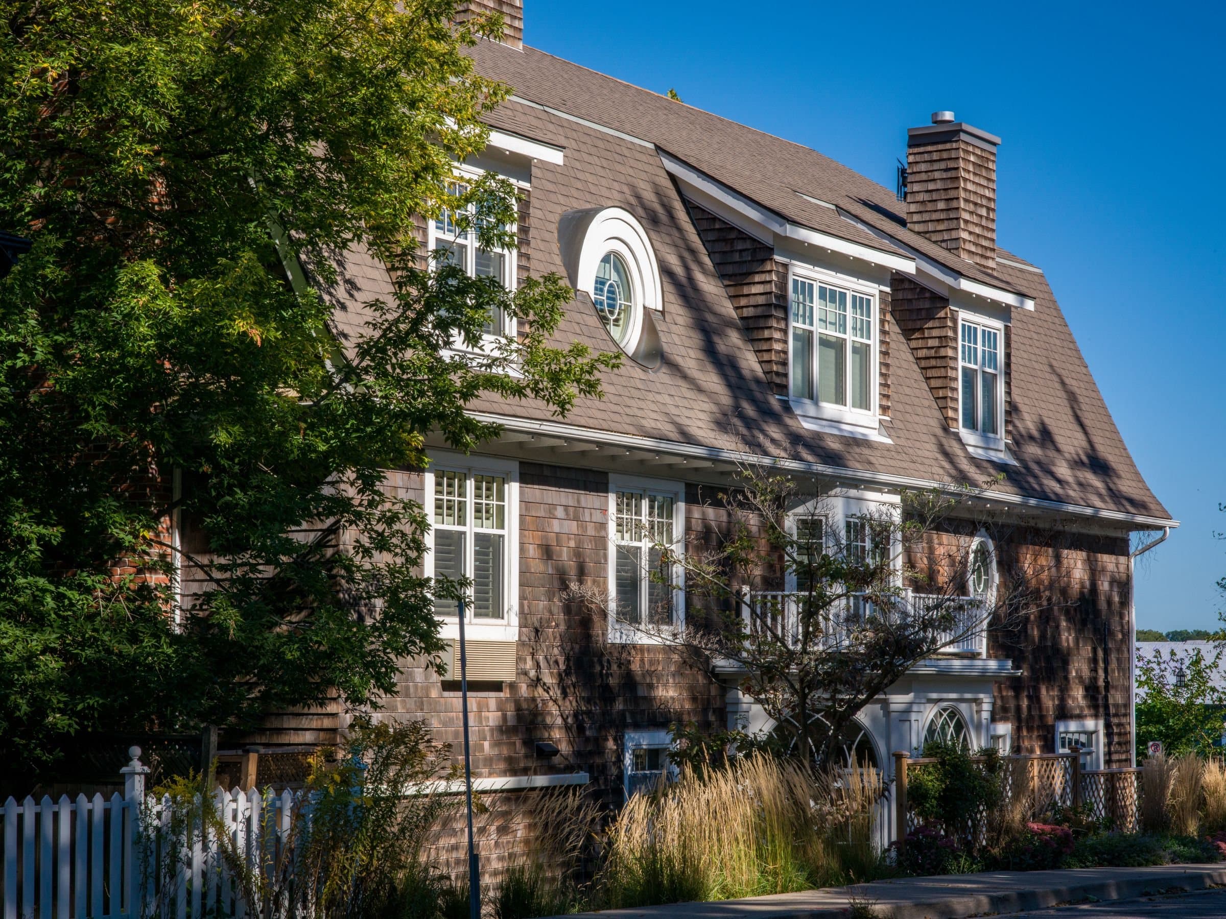 Rye, NY: a shingled two-story house with dormers and a white fence on a sunny day